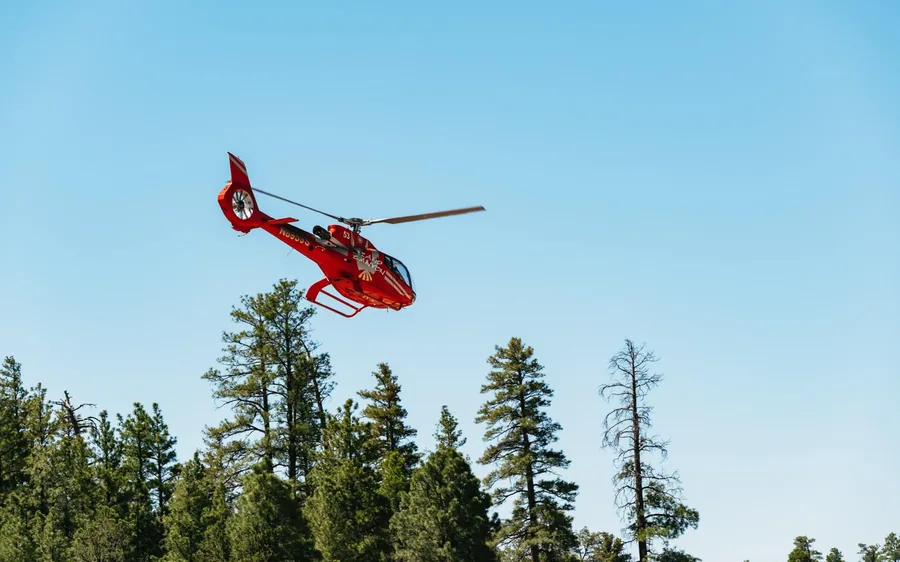 A red helicopter climbing over the Kaibab forest at the Grand Canyon